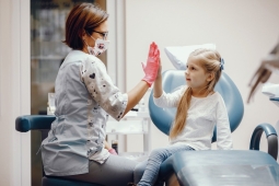 Eine junge Zahnärztin und ein Mädchen mit langen Haaren geben sich ein High Five