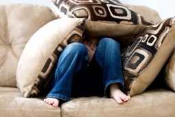Ein Junge sitzt auf dem Sofa und hat sich mit Kissen einen Schutz gebaut