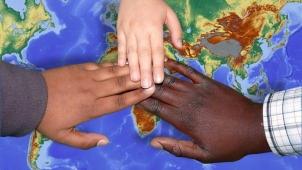 Drei Kinderhände verschiedener Hautfarben liegen übereinander, darunter eine Weltkarte
